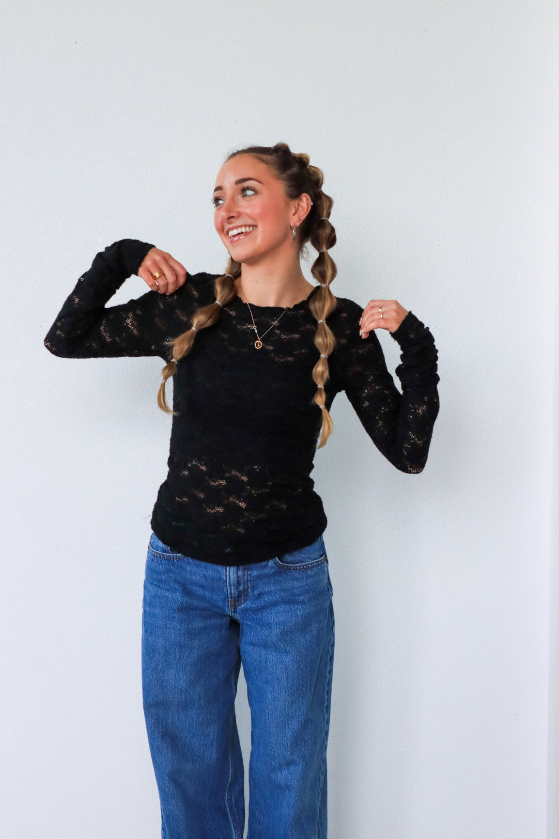 Woman wearing a black lace top and blue jeans against a white background