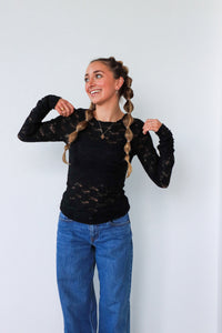 Woman wearing a black lace top and blue jeans against a white background