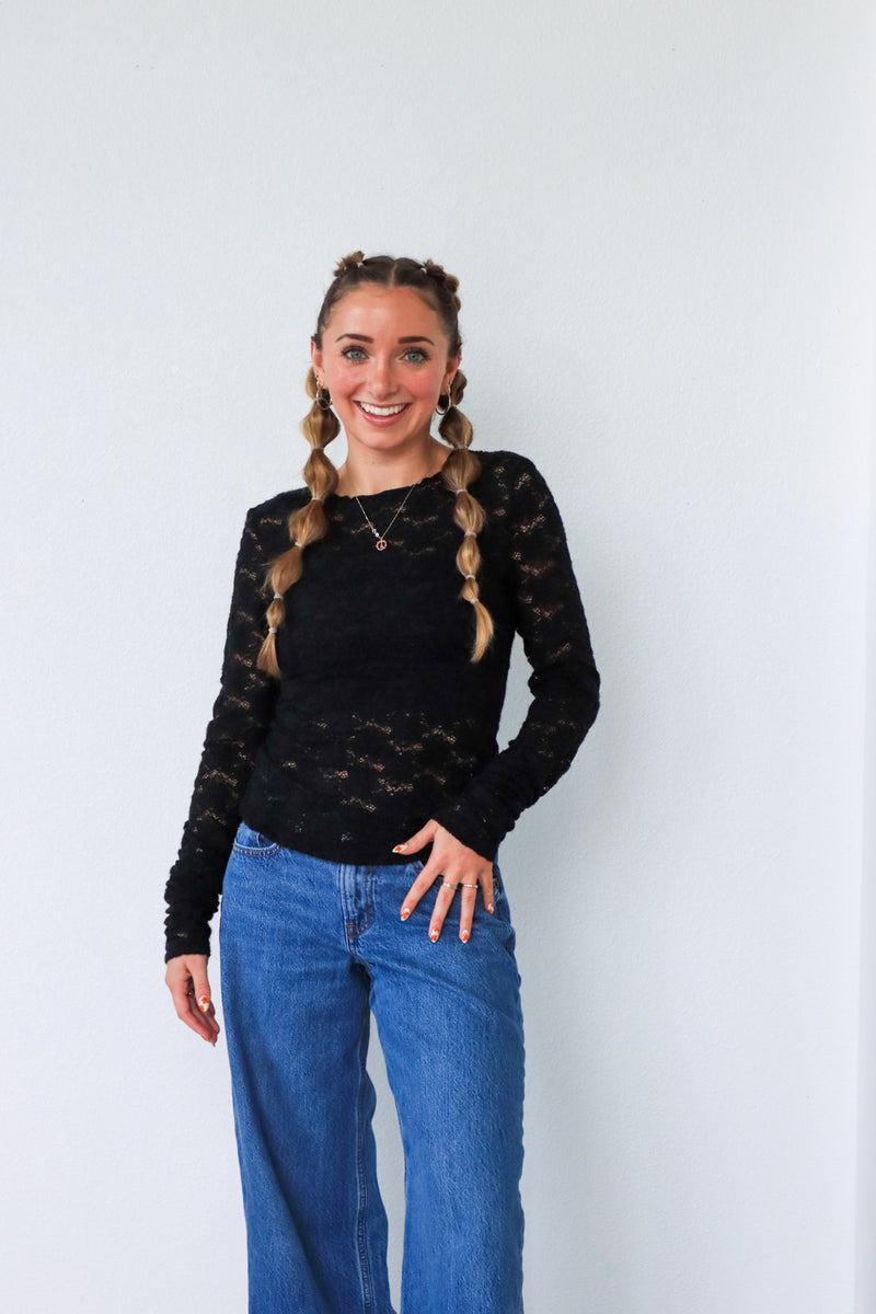 Woman wearing a black lace top and blue jeans against a white background