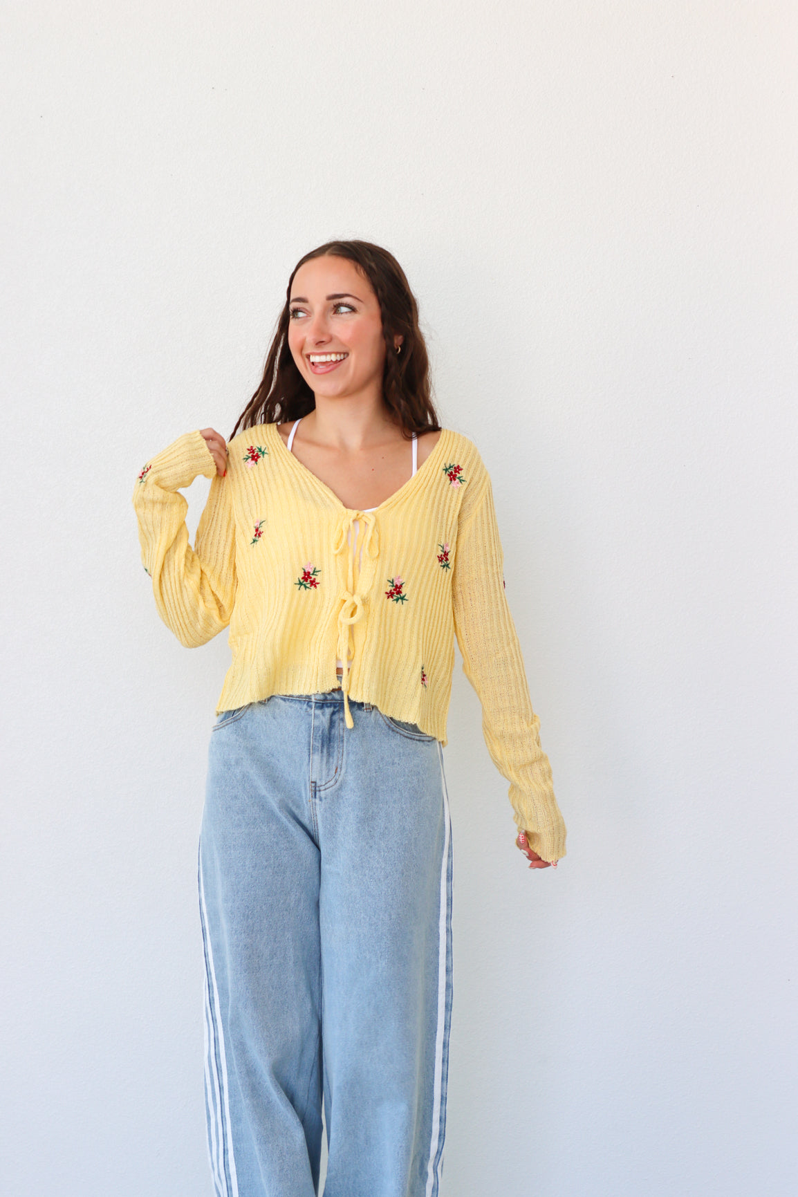 Woman wearing a yellow embroidered blouse and blue jeans against a white background