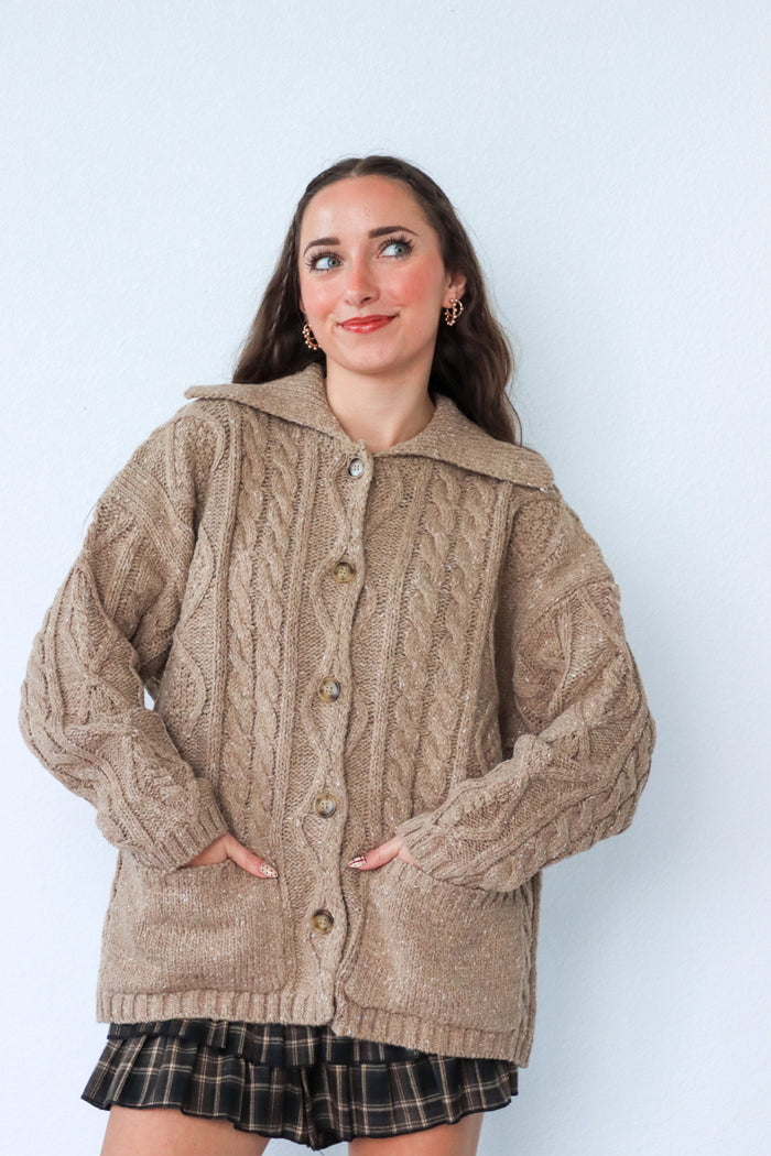 Woman wearing a beige knitted cardigan against a light blue background