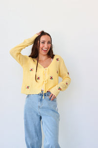 Woman wearing a yellow cardigan with floral embroidery against a white background