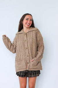 Woman wearing a beige cardigan with a hood against a white background