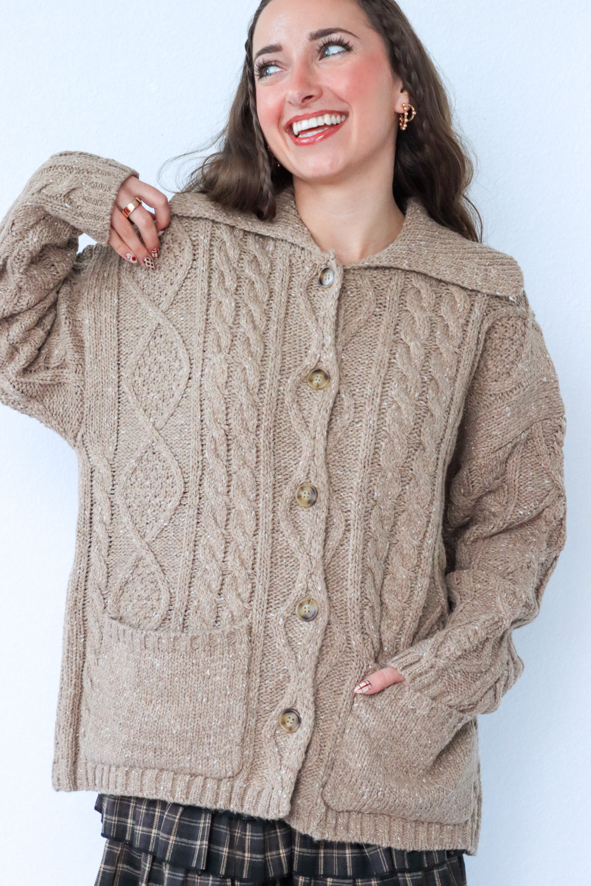 Woman wearing a beige cable knit cardigan against a white background