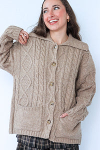 Woman wearing a beige cable knit cardigan against a white background