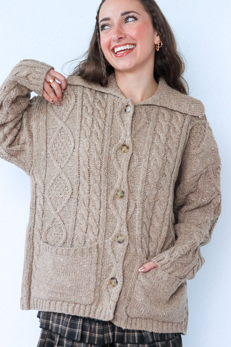 Woman wearing a beige cable knit cardigan against a white background