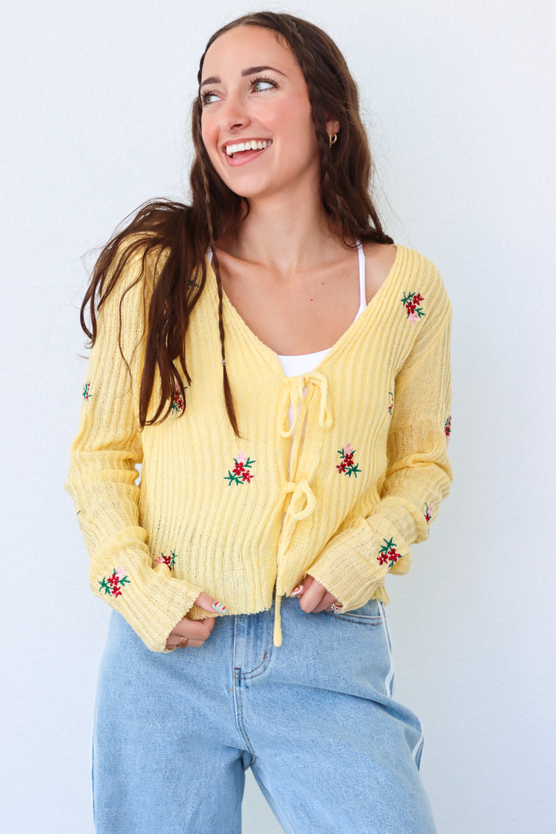 Woman wearing a yellow cardigan with floral embroidery against a white background
