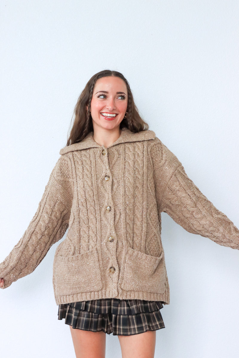 Woman wearing a beige knitted cardigan with a plaid skirt against a white background
