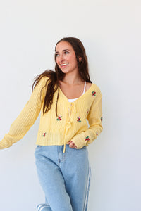 Woman wearing a yellow cardigan with floral embroidery against a white background
