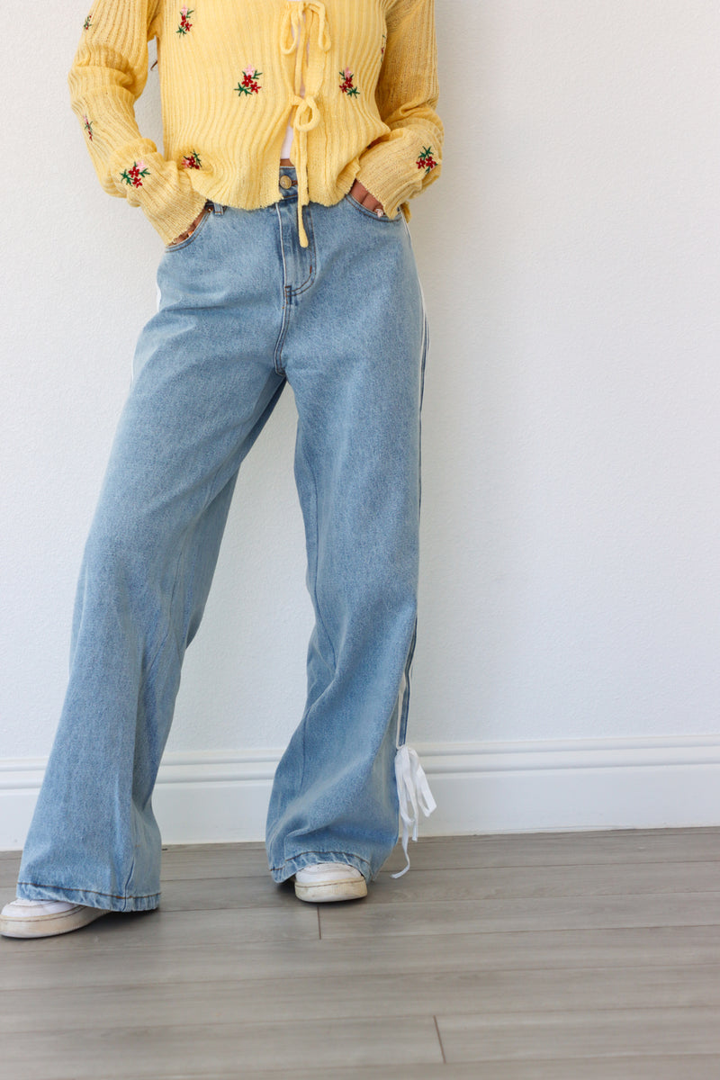 Person wearing a yellow embroidered sweater and blue jeans against a white wall.