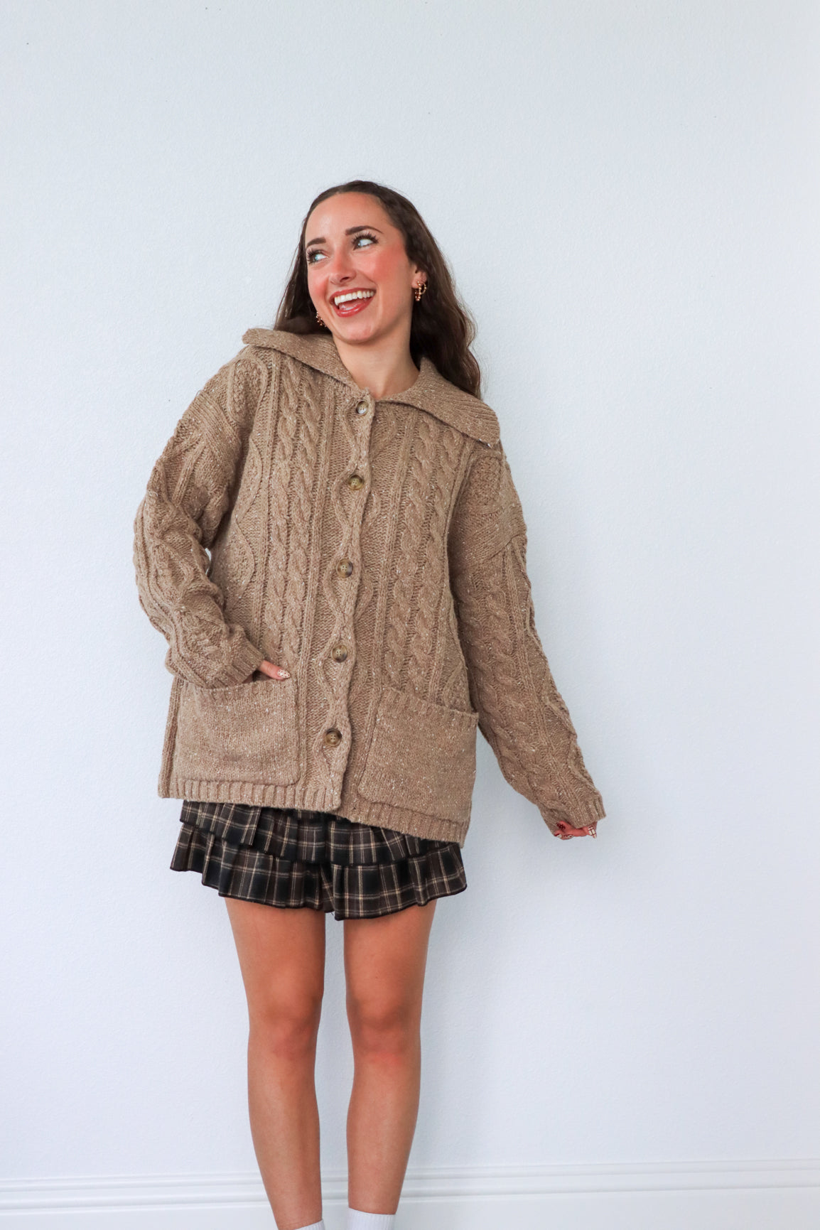 Woman wearing a brown cable knit cardigan against a white background