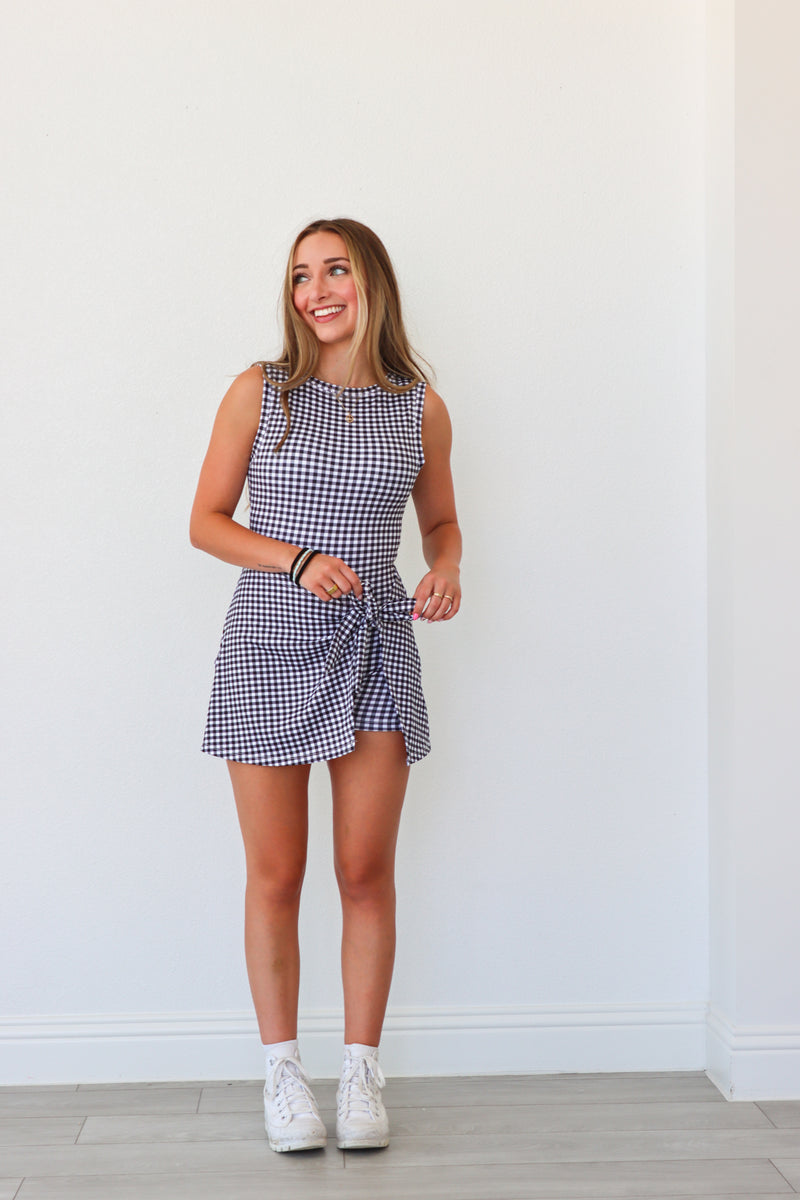 Woman wearing a checkered dress standing against a white wall