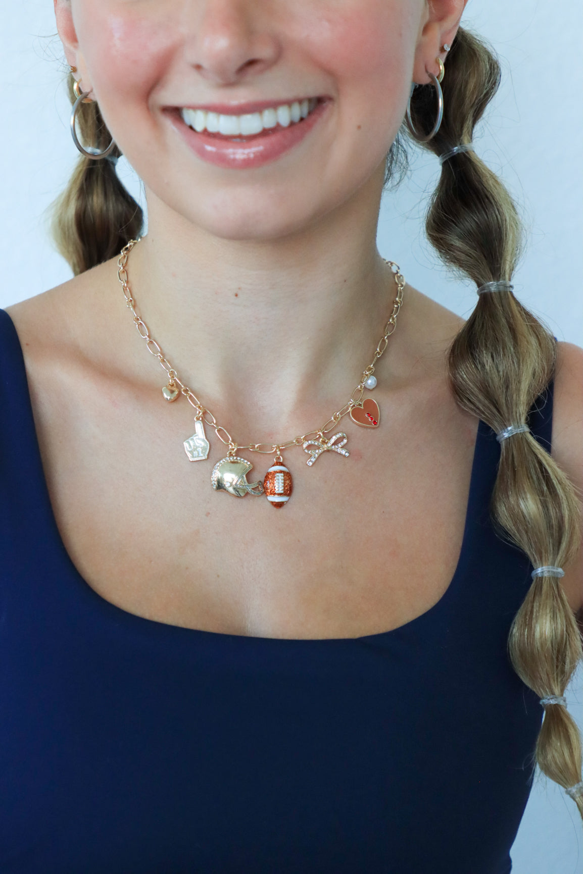 Person wearing a necklace with various charms against a plain background