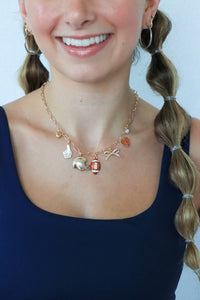 Person wearing a necklace with various charms against a plain background