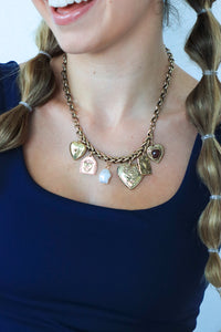 Person wearing a gold necklace with heart-shaped charms against a plain background