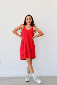 Woman wearing a red dress standing against a white wall.