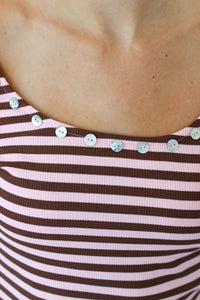 Close-up of a person wearing a ribbed top with horizontal brown and pink stripes and small decorative buttons along the neckline.