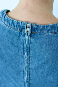 Close-up of the back neckline of a blue denim garment, showing a silver metal zipper running down the center.