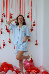 Woman in light blue pajama set standing in front of a wall with red decorations and heart-shaped balloons on the floor.