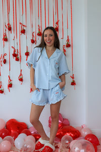 Woman in light blue pajama set standing in front of a decorative wall with red ribbons and balloons.