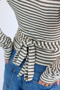 Close-up of a person wearing a cream and gray striped long-sleeve top tied at the waist, paired with blue jeans.