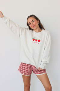 girl wearing light gray crewneck that has an embroidered strawberry "thank you berry much" graphic