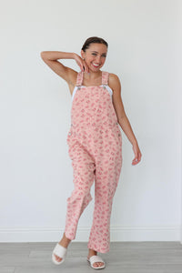 girl wearing long light pink overalls with a floral pattern