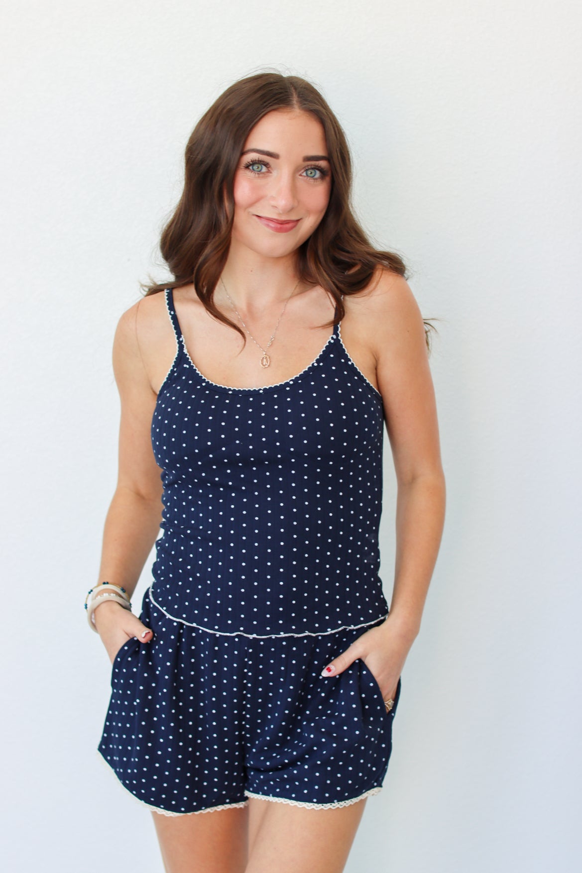 A woman modeling a navy blue tank and shorts set with white polka dots and white trim, standing against a plain white background.