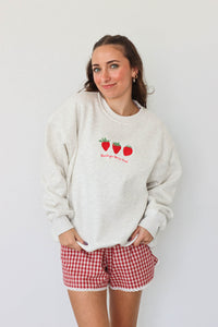 girl wearing light gray crewneck that has an embroidered strawberry "thank you berry much" graphic