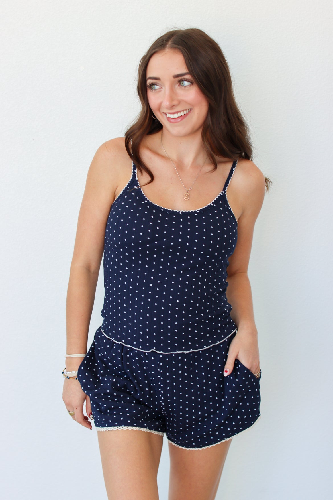 A woman modeling a navy blue tank and shorts set with white polka dots and white trim, standing against a plain white background.