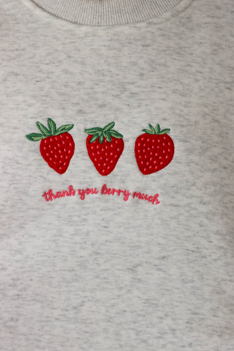 girl wearing light gray crewneck that has an embroidered strawberry "thank you berry much" graphic