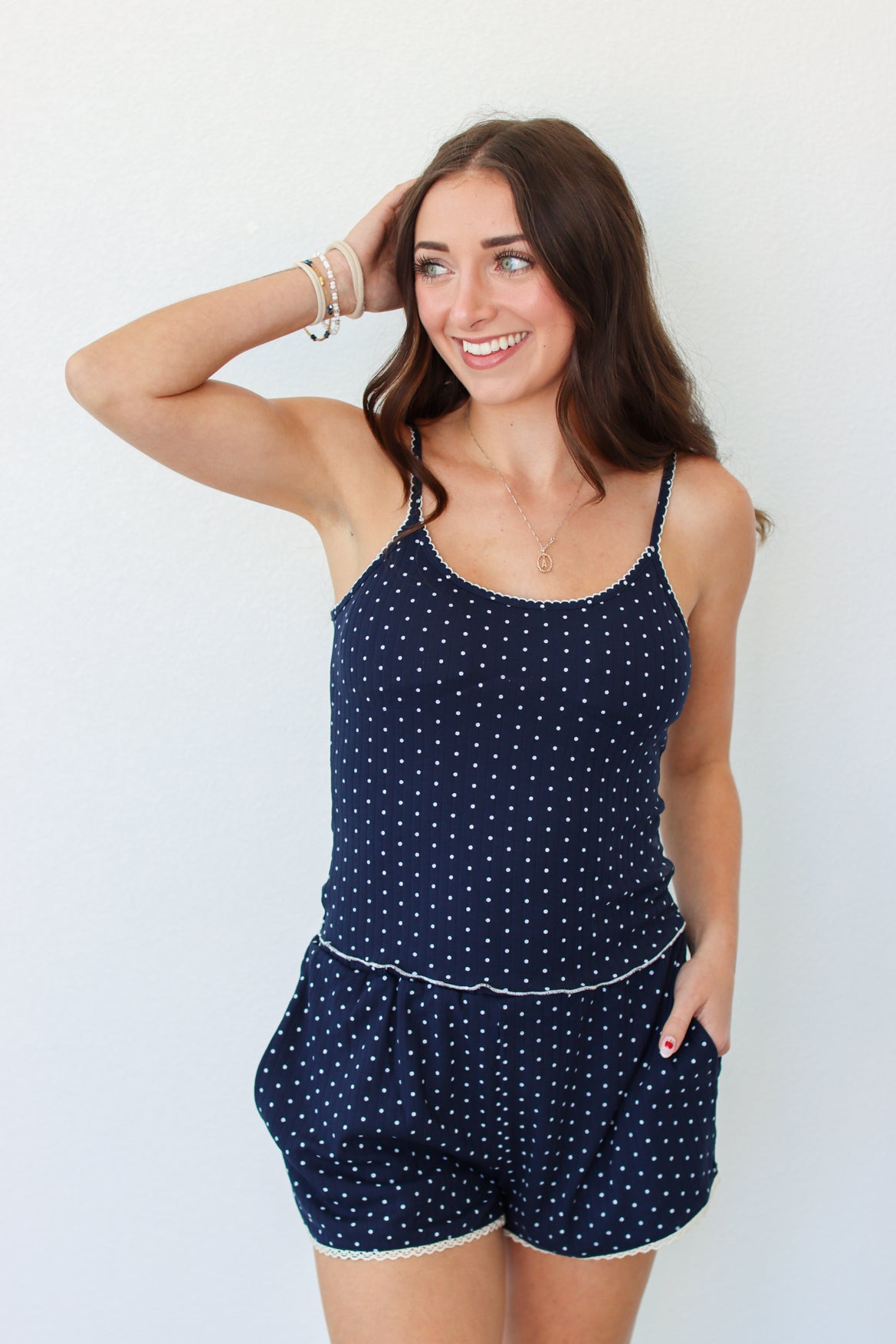 A woman modeling a navy blue tank and shorts set with white polka dots and white trim, standing against a plain white background.