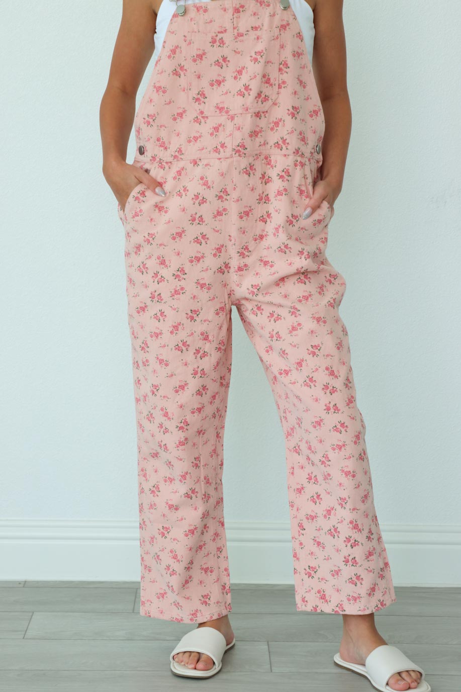girl wearing long light pink overalls with a floral pattern