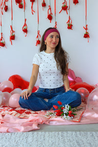 Woman sitting on a floor decorated with balloons and flowers, surrounded by red ribbons and flowers.