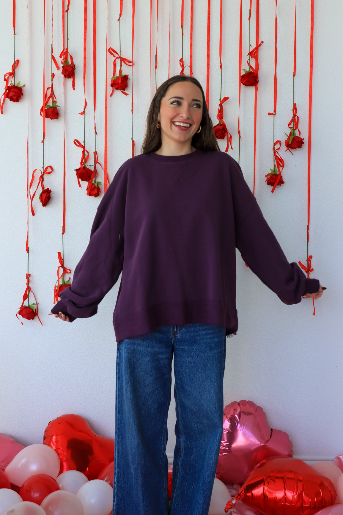 Woman in a purple sweater standing in front of a decorative wall with red ribbons and balloons.