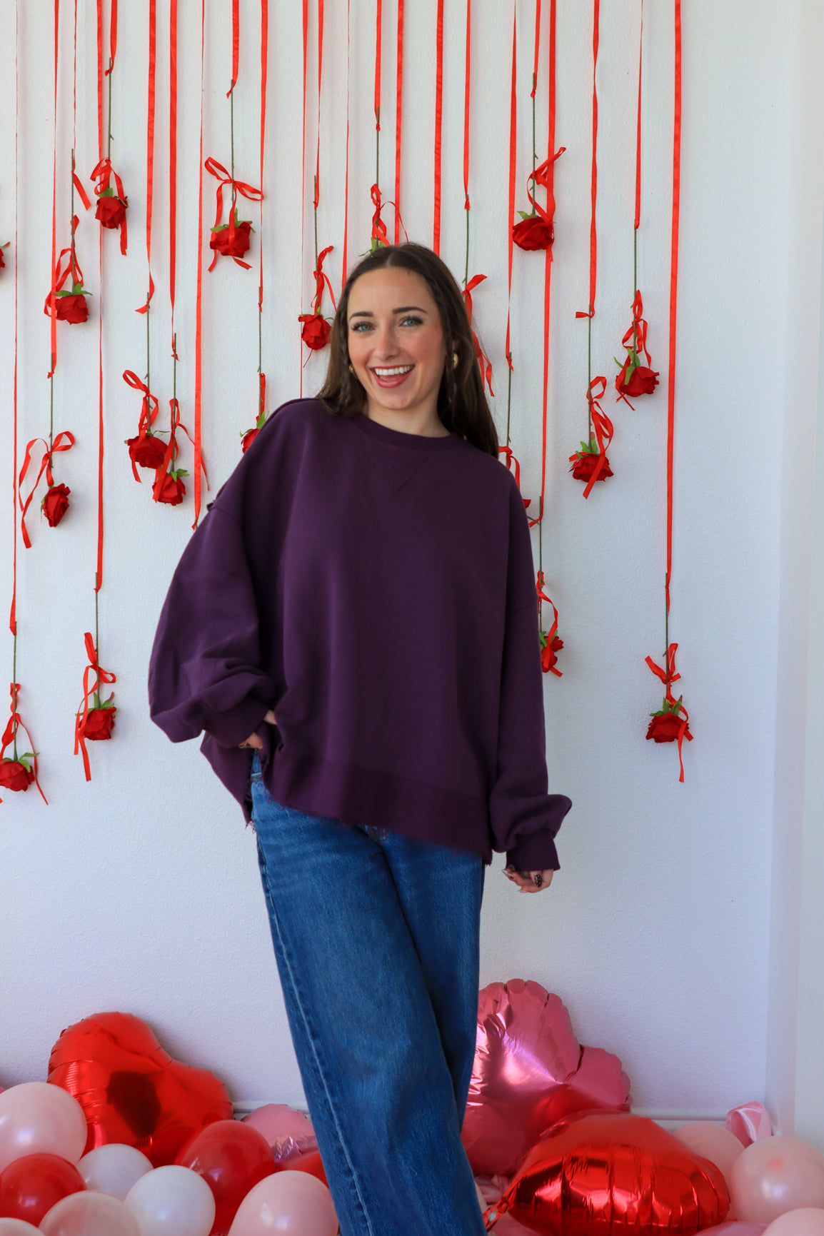 Woman in a purple sweater standing in front of a decorative wall with red ribbons and balloons.