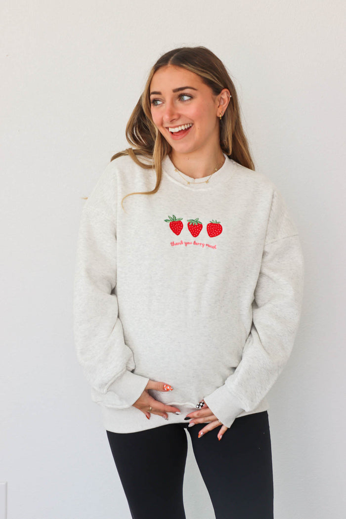 girl wearing light gray crewneck that has an embroidered strawberry "thank you berry much" graphic