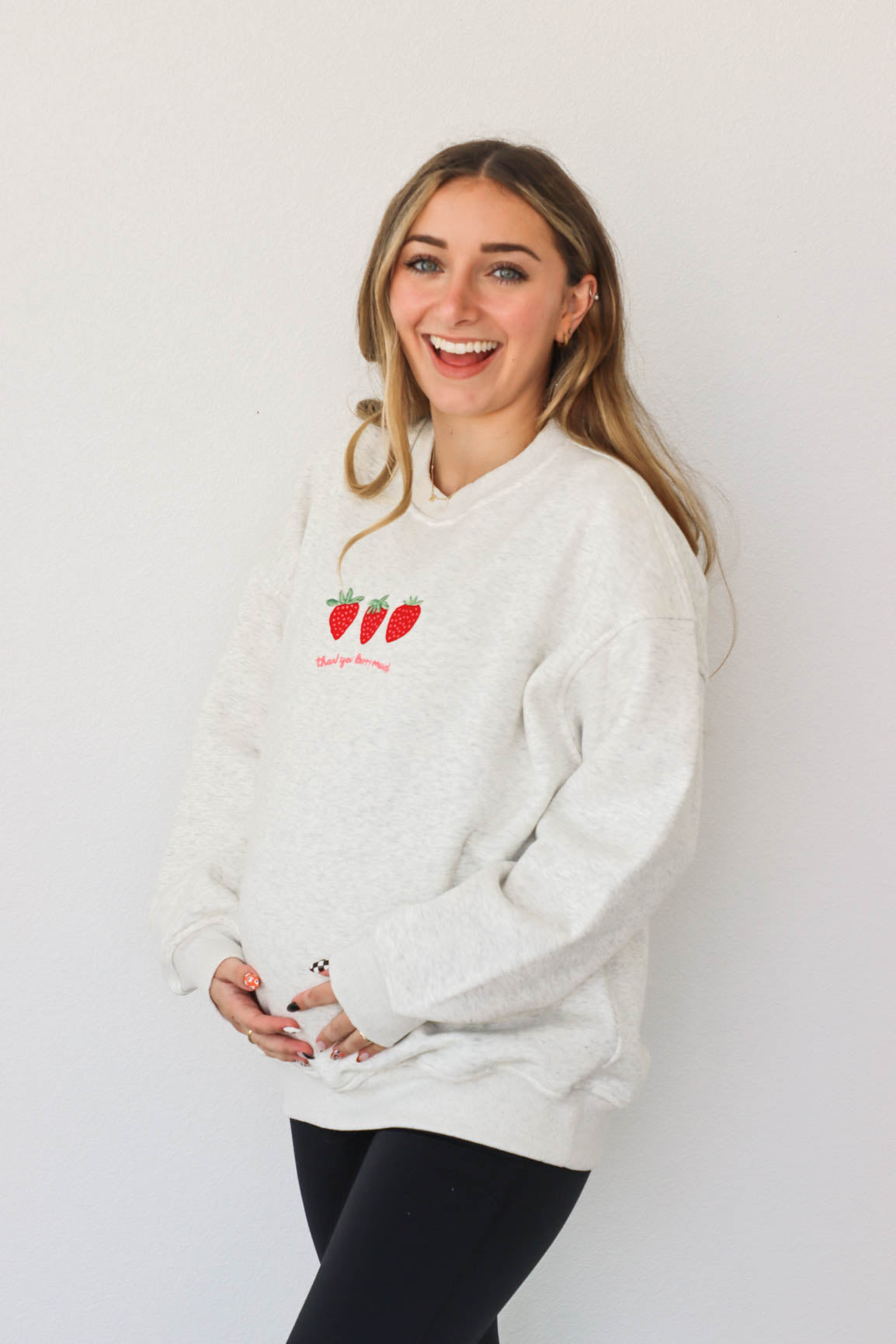 girl wearing light gray crewneck that has an embroidered strawberry "thank you berry much" graphic