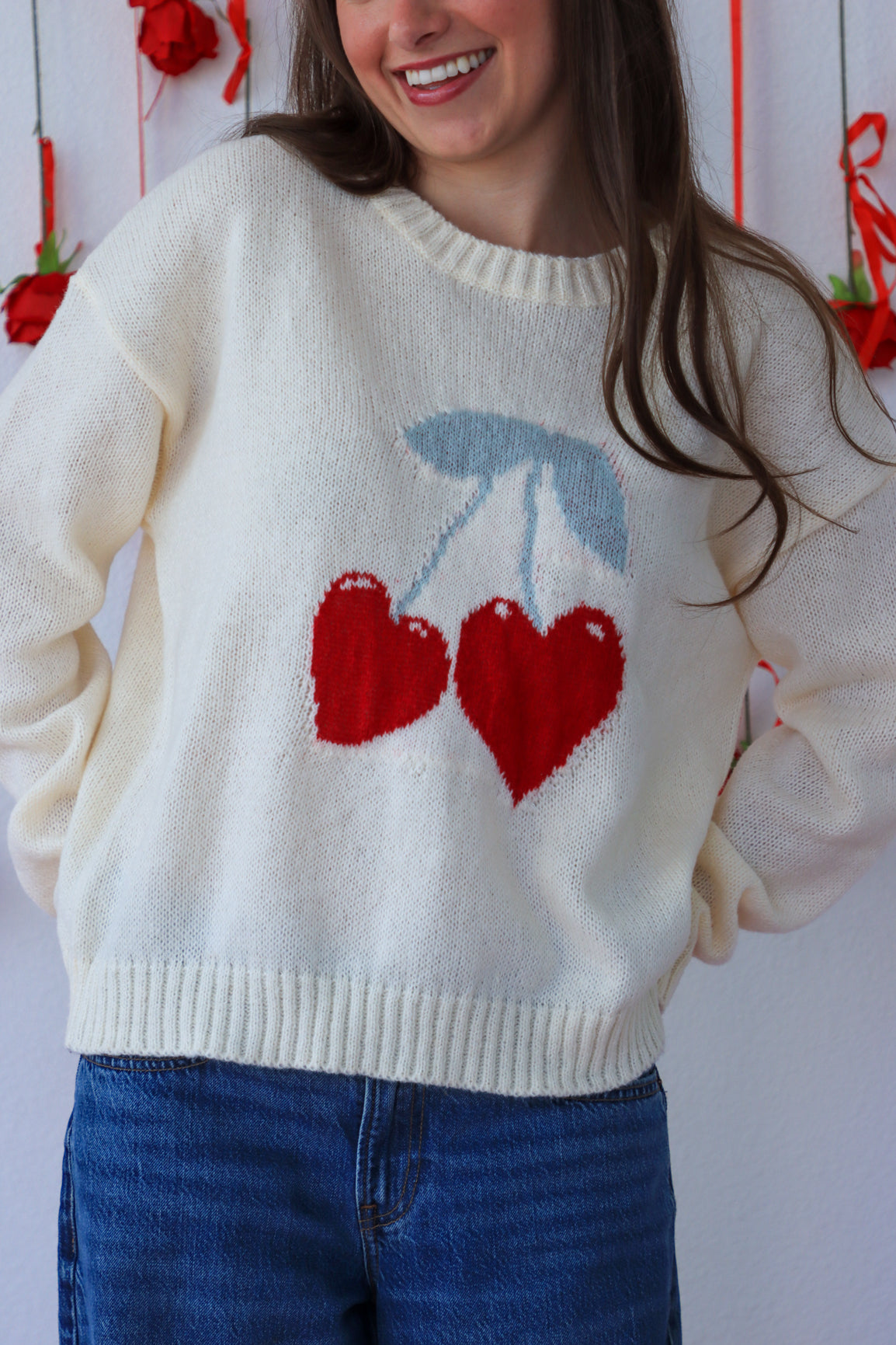 Person wearing a cream sweater with red heart design against a white background