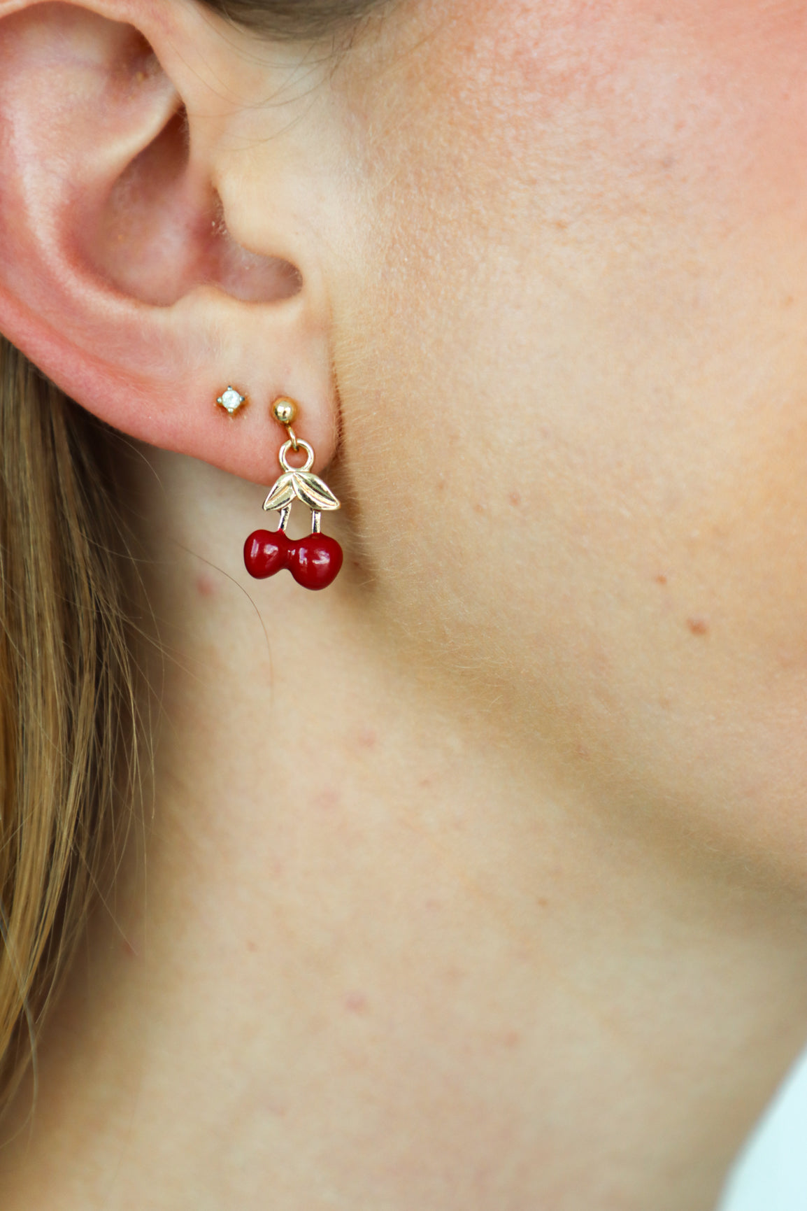 Close-up of a person wearing gold earrings with red berry charms.