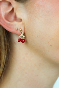 Close-up of a person wearing gold earrings with red berry charms.