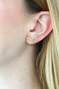 Gold bow-shaped earring worn by a person with blonde hair.