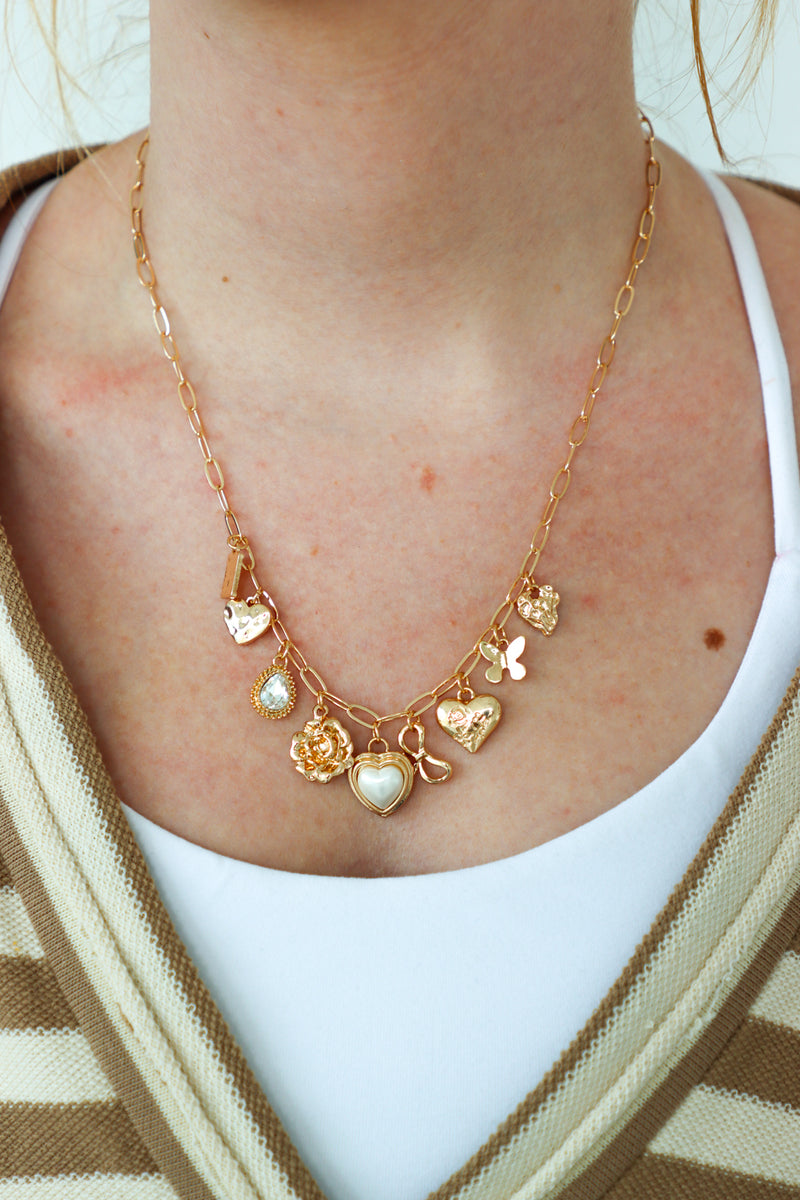 Gold necklace with heart and flower charms worn by a person