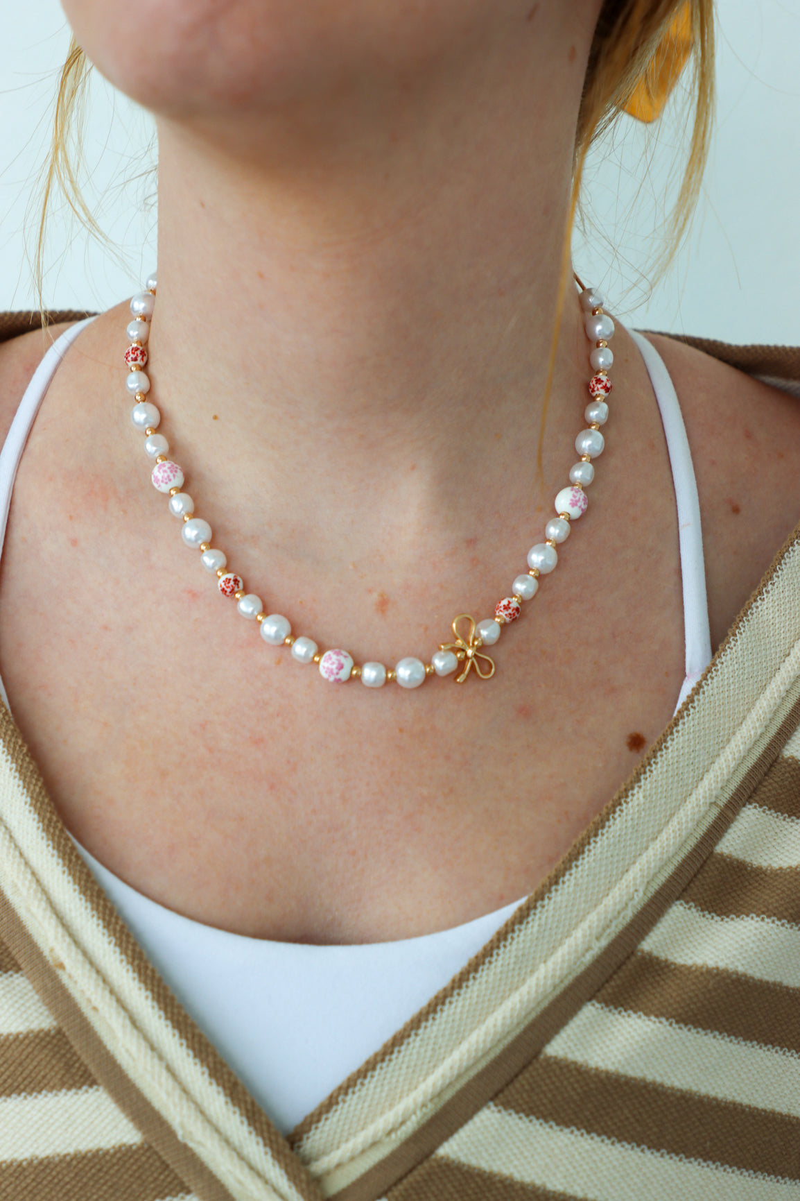 Person wearing a pearl necklace with a white top and striped cardigan.