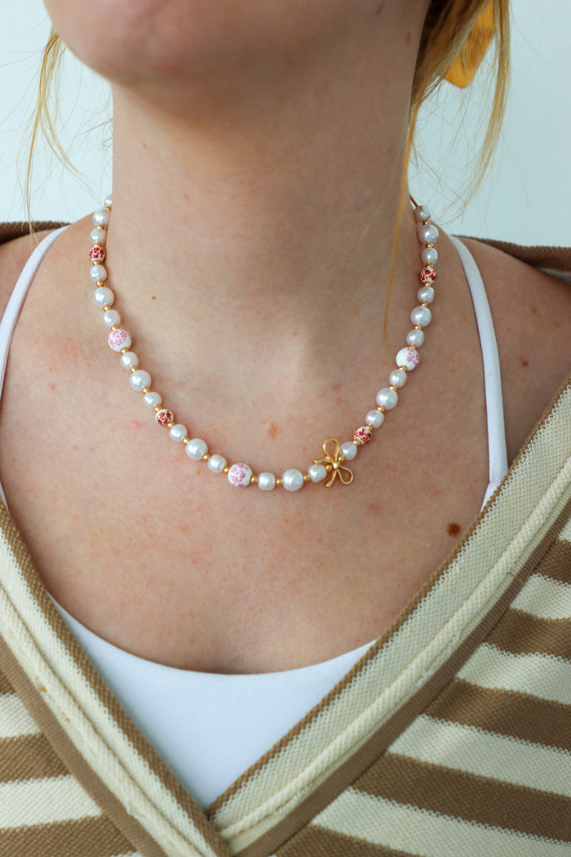Person wearing a pearl necklace with a white top and striped cardigan.