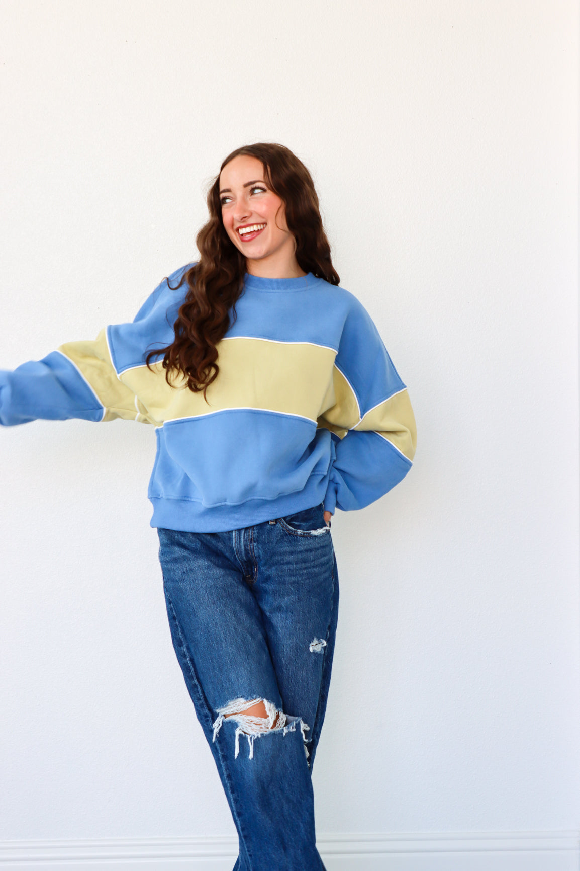 Woman wearing a blue and yellow sweater with ripped jeans against a white background