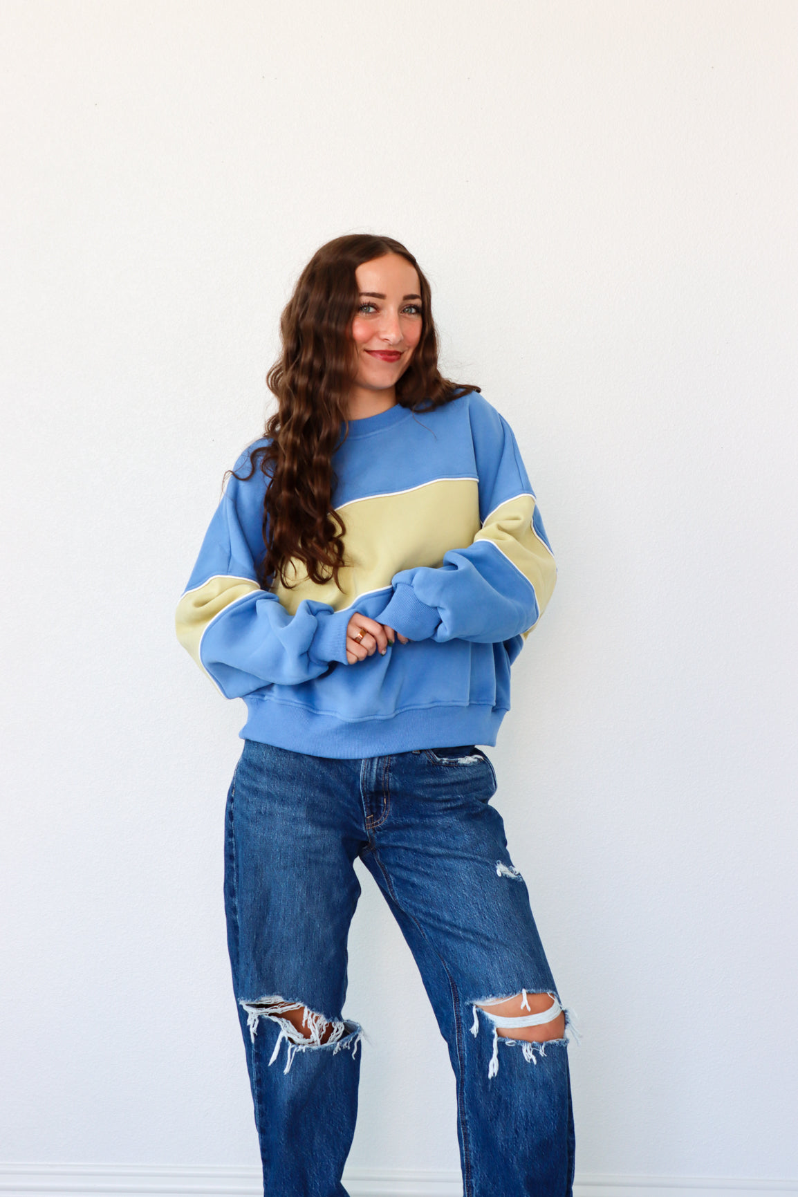 Woman wearing a blue and yellow sweater with ripped jeans against a white background