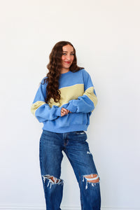 Woman wearing a blue and yellow sweater with ripped jeans against a white background