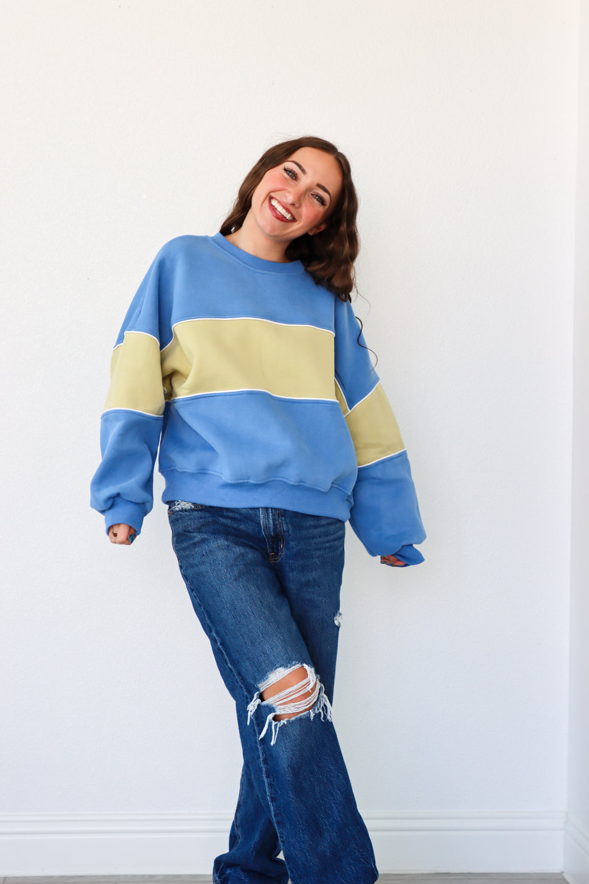 Woman wearing a blue and beige sweater with ripped jeans against a white background