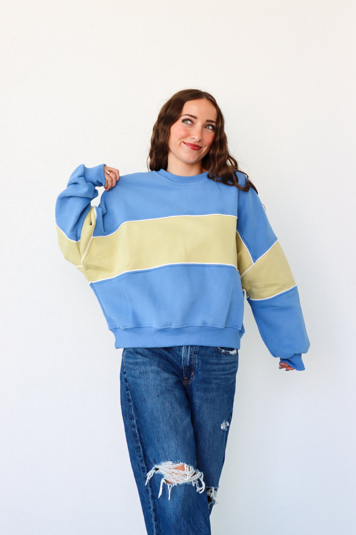 Person wearing a blue and beige striped sweater with ripped jeans on a white background